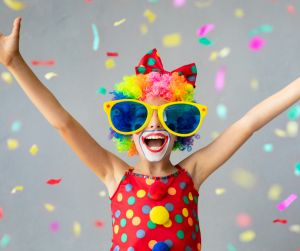 kid dressed as clown with big glasses, big smile and arms up