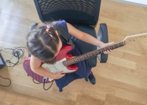 kid playing electric guitar while seated