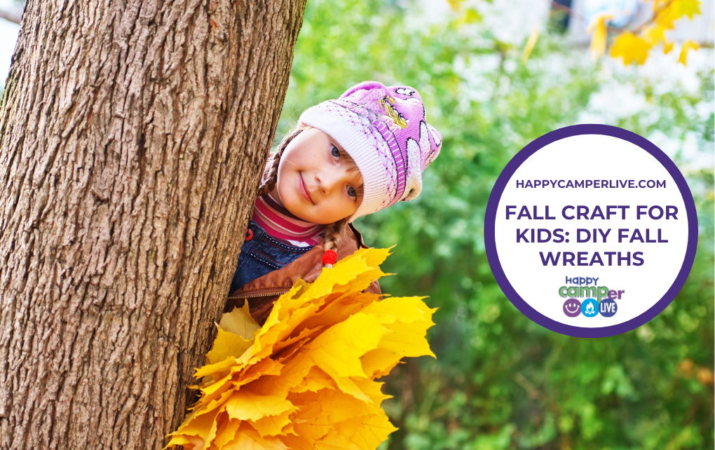 a child peeks out from behind a tree while holding fall leaves