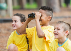 three kids, child in middle is using binoculars