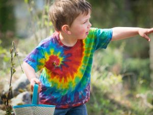 a child wearing a tie dye shirt holds a basket and points