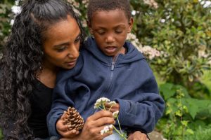  a child holds a pinecone. A parent holds the child